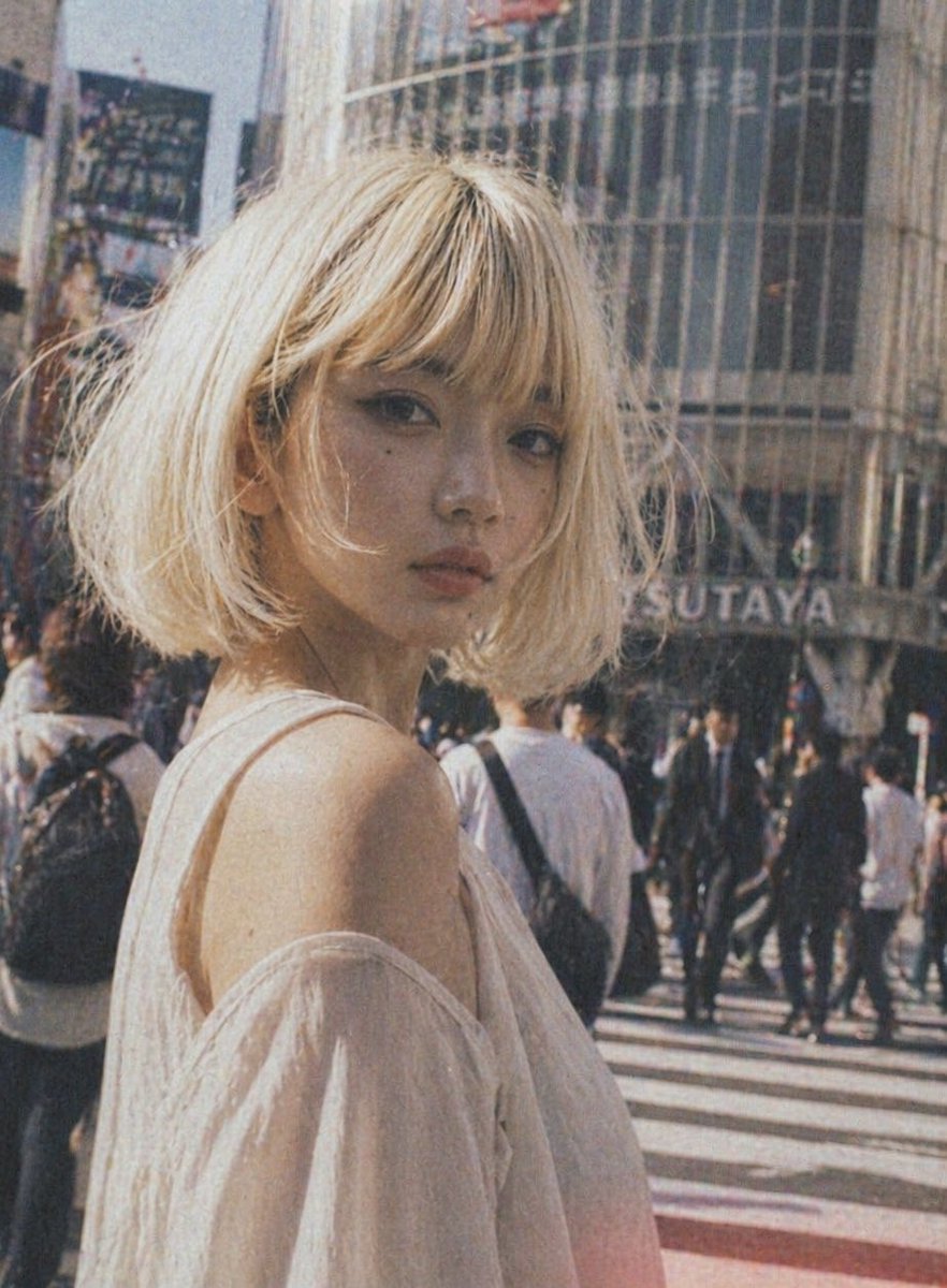 A candid street-fashion portrait of a young woman standing at a busy Tokyo crosswalk in daylight, framed from the upper…