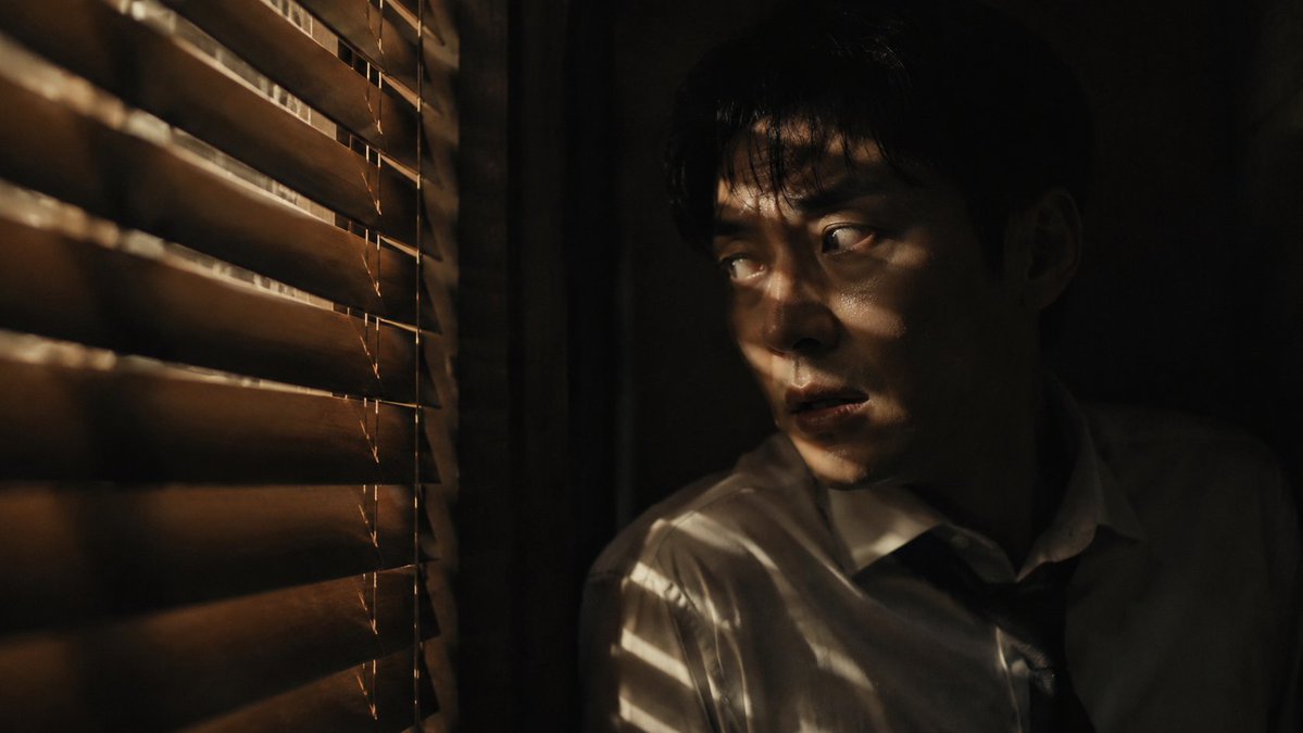 Create a dark cinematic thriller film still of a {argument name="subject" default="East Asian man"} hiding in a narrow …