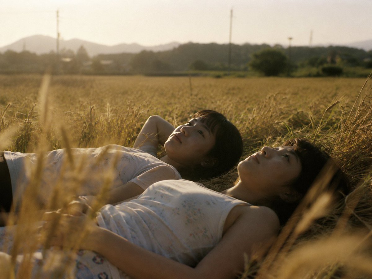 Create a cinematic, realistic 4:3 landscape photograph of two young people lying on their backs in a dry golden wheat f…