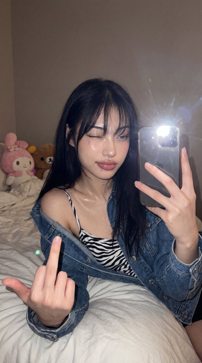 A high-angle front-camera phone selfie of a young woman in her 20s sitting or half-lying on a {argument name="backgroun…