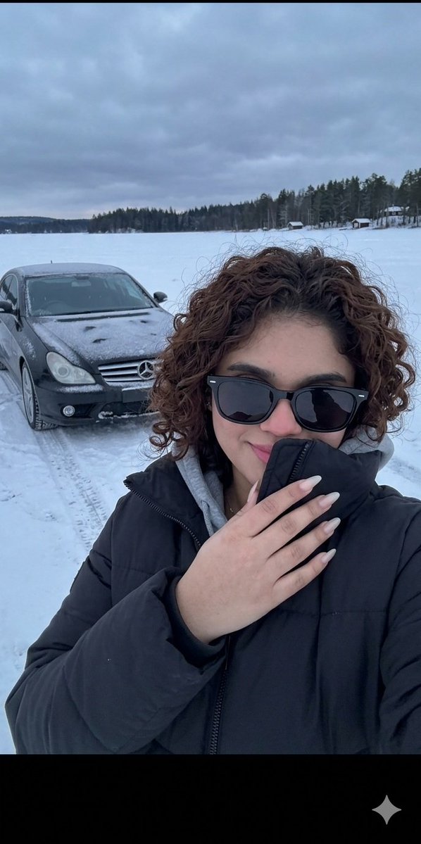 A young woman wearing a {argument name="clothing" default="black winter puffer jacket and a gray hoodie"} is taking a s…